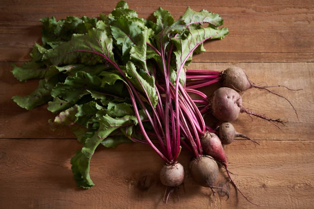 A bunch of freshly picked beets with their greens on a wooden surface.
