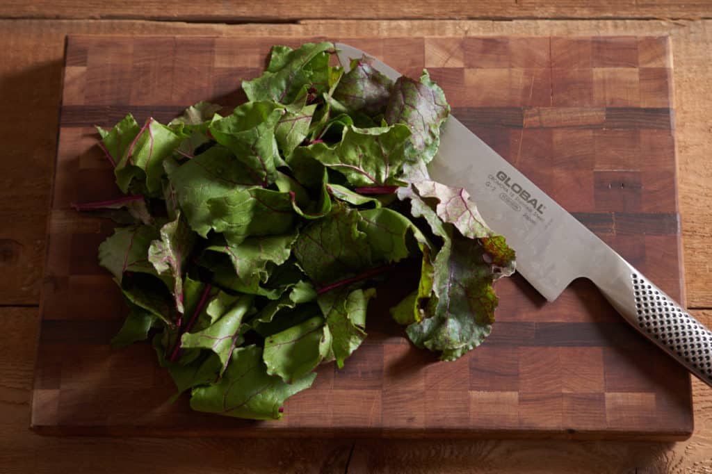 A chef's knife on a cutting board with chopped beet leaves.