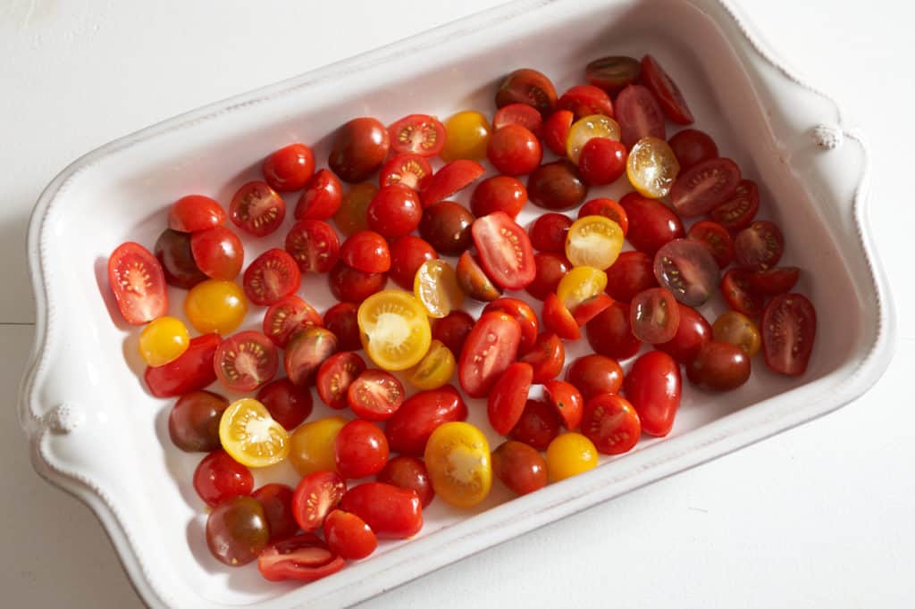 Sliced red and yellow cherry tomatoes in a white casserole dish.