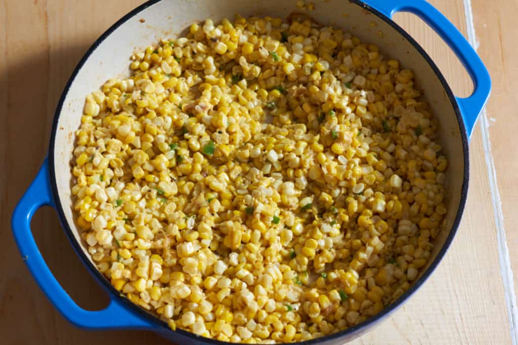 A blue casserole pan with corn kernels and serrano chiles.