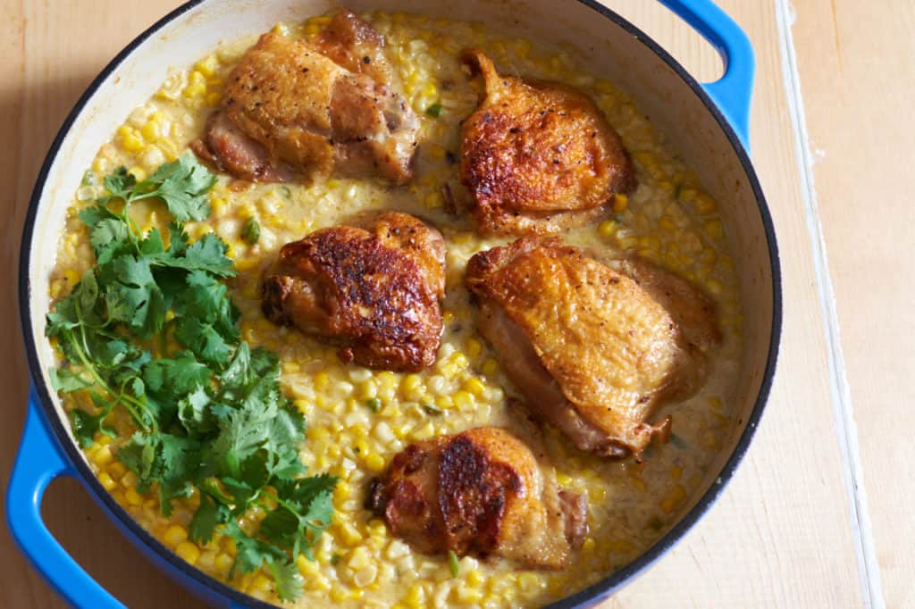 Chicken thighs with coconut milk creamed corn and cilantro in a blue casserole pan.