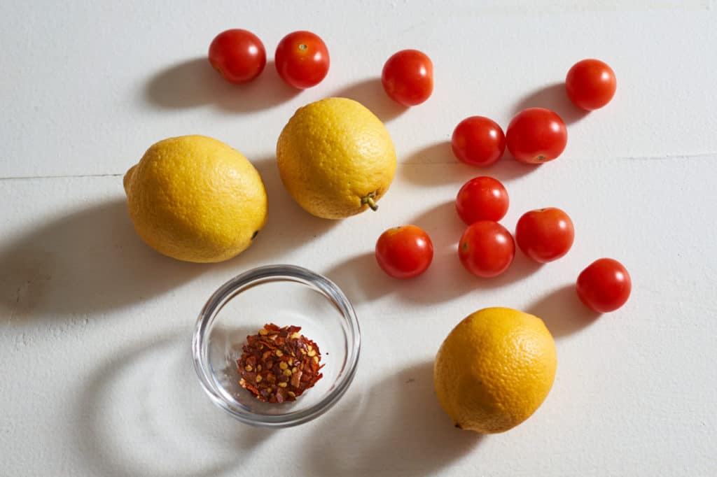 Lemons, cherry tomatoes, and a small bowl of crushed red pepper.