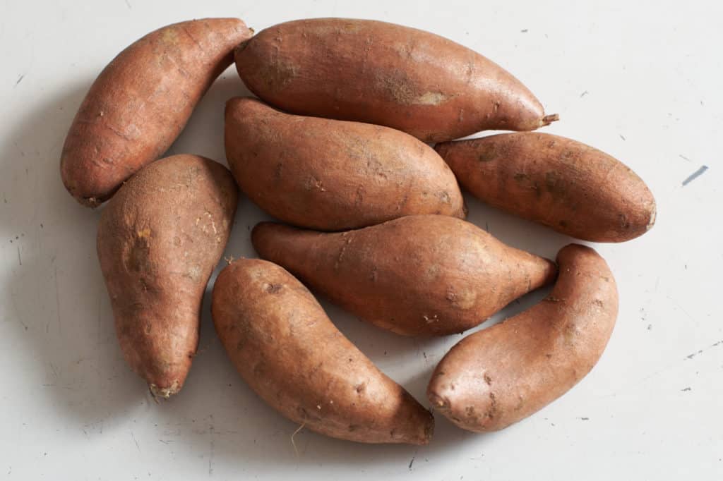 Whole sweet potatoes on a white surface.