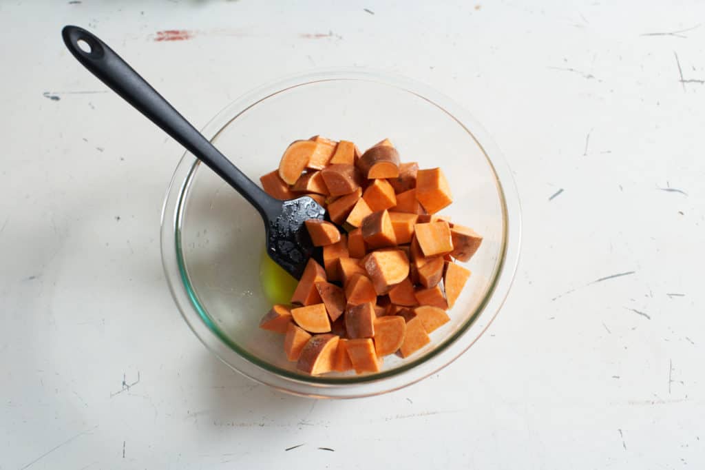 A spatula sits in a glass bowl filled with diced sweet potatoes.