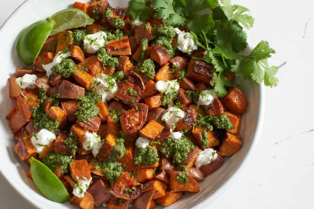 Oven roasted sweet potatoes with chile lime cilantro sauce in a white bowl.