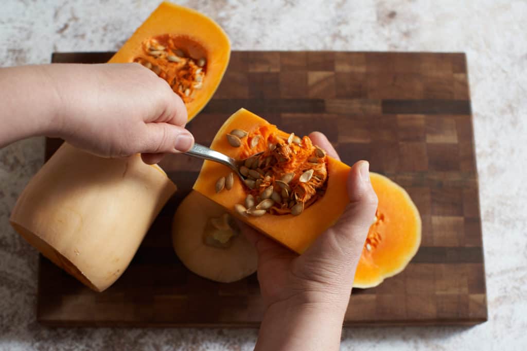 A woman's hands are shown scooping the seeds from a butternut squash.