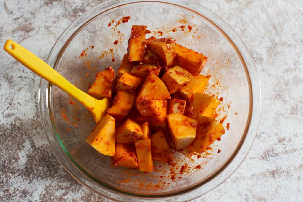 A glass bowl containing chopped butternut squash mixed with harissa.