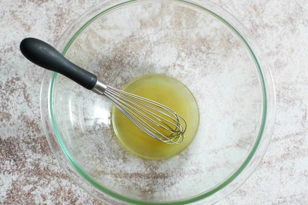 A glass bowl of salad dressing with a whisk in it.