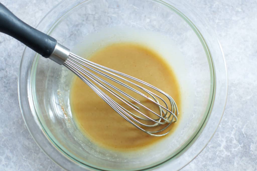 A whisk sits in a bowl of tahini sauce.