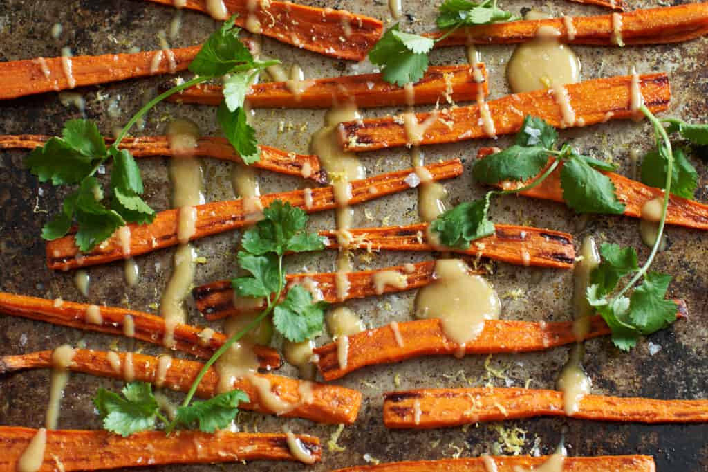 Oven roasted carrots with tahini sauce and cilantro on a baking sheet.