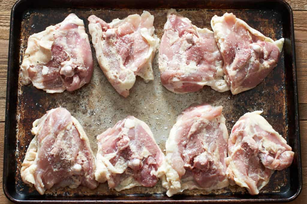Raw chicken thighs on a sheet pan.