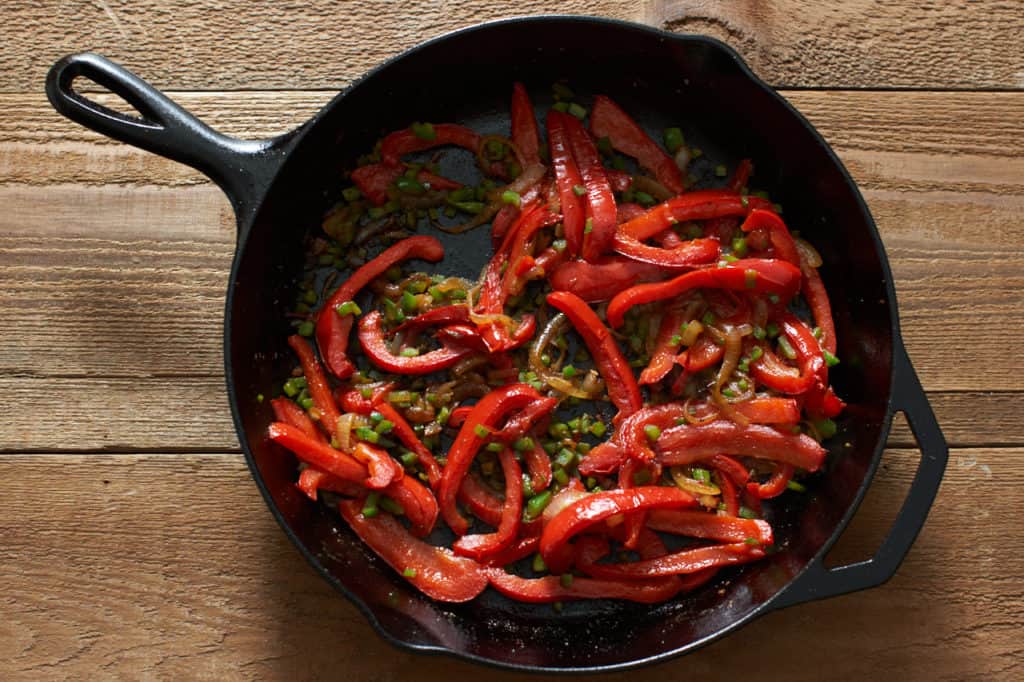 A cast iron skillet with sautéed onions, red bell peppers, and jalapeños.