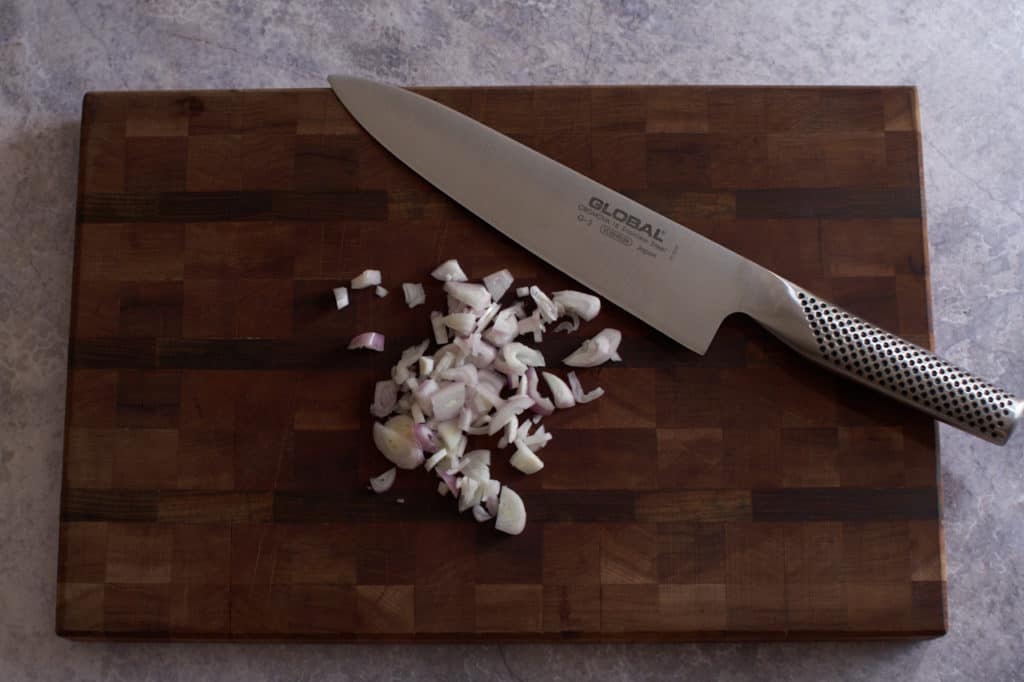 Chopped shallots and a chef's knife on a cutting board.