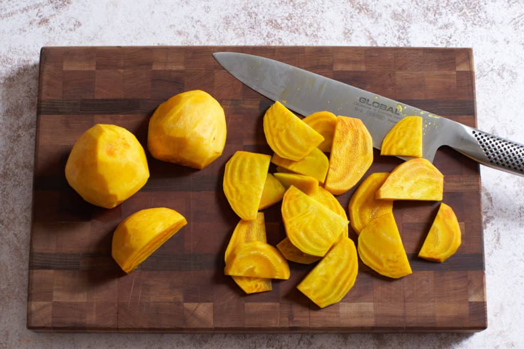 Sliced golden beets and a chef's knife on a wooden cutting board.
