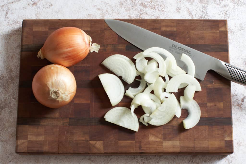 Sliced onions and a chef's knife on a wooden cutting board.