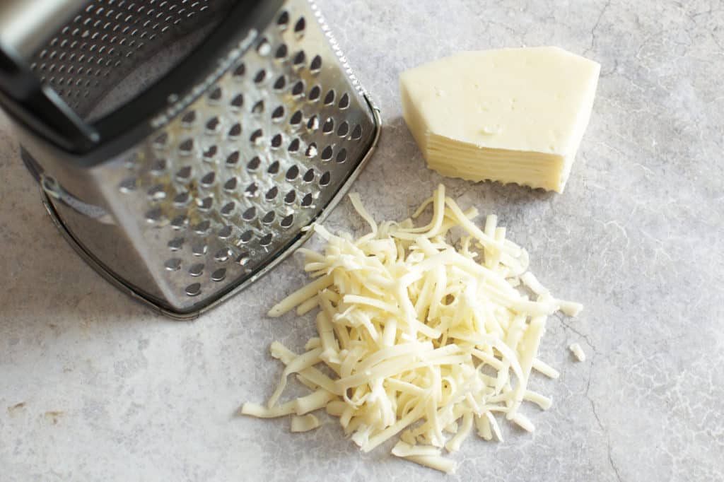 A box grater next to grated fontina cheese.