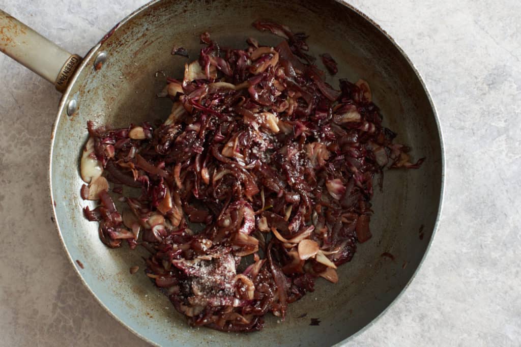 Caramelized red onions in a skillet with sliced garlic and radicchio.