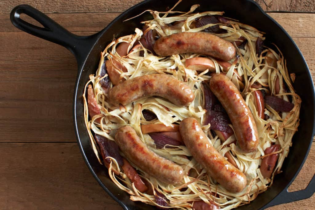 Oven baked italian sausage with apples, parsnips and onions in a cast iron skillet.