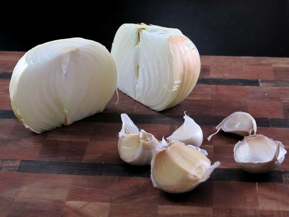 A sliced onion and several garlic cloves on a cutting board.