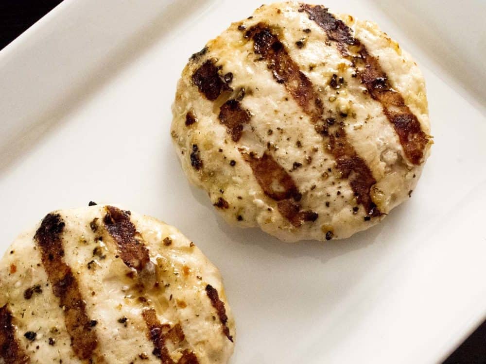 Two finished turkey burger patties with grill marks on a white plate.