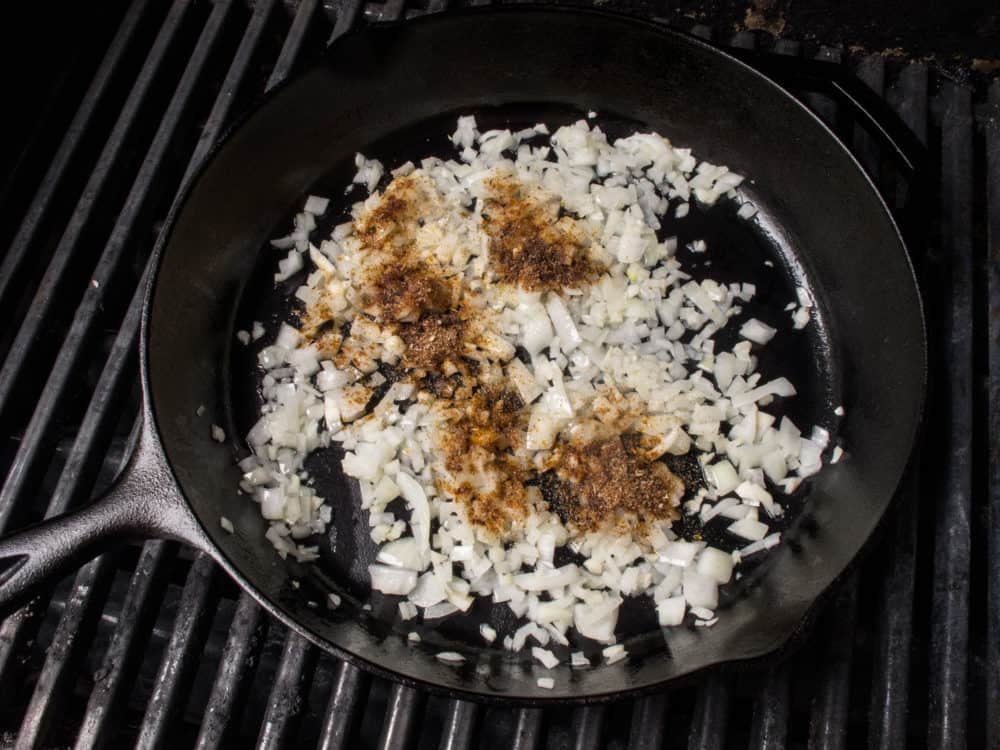 Onions cooking in a cast iron skillet on a grill. 