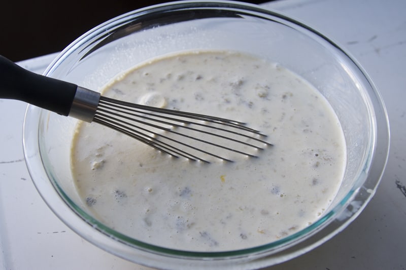 A whisk in a glass bowl with cream and mashed bananas.