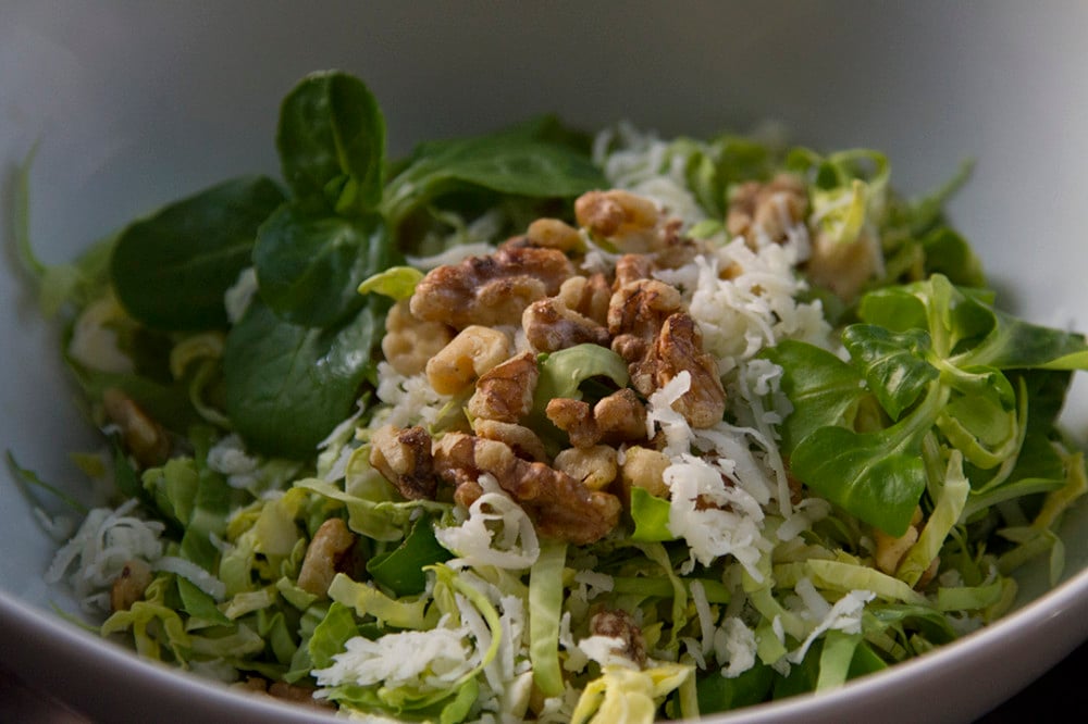 Shaved brussels sprouts salad topped with walnuts and cheese in a white bowl. 