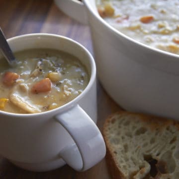 A cup of chicken pot pie soup pictured next to a pot of the soup and with a side of toasted bread