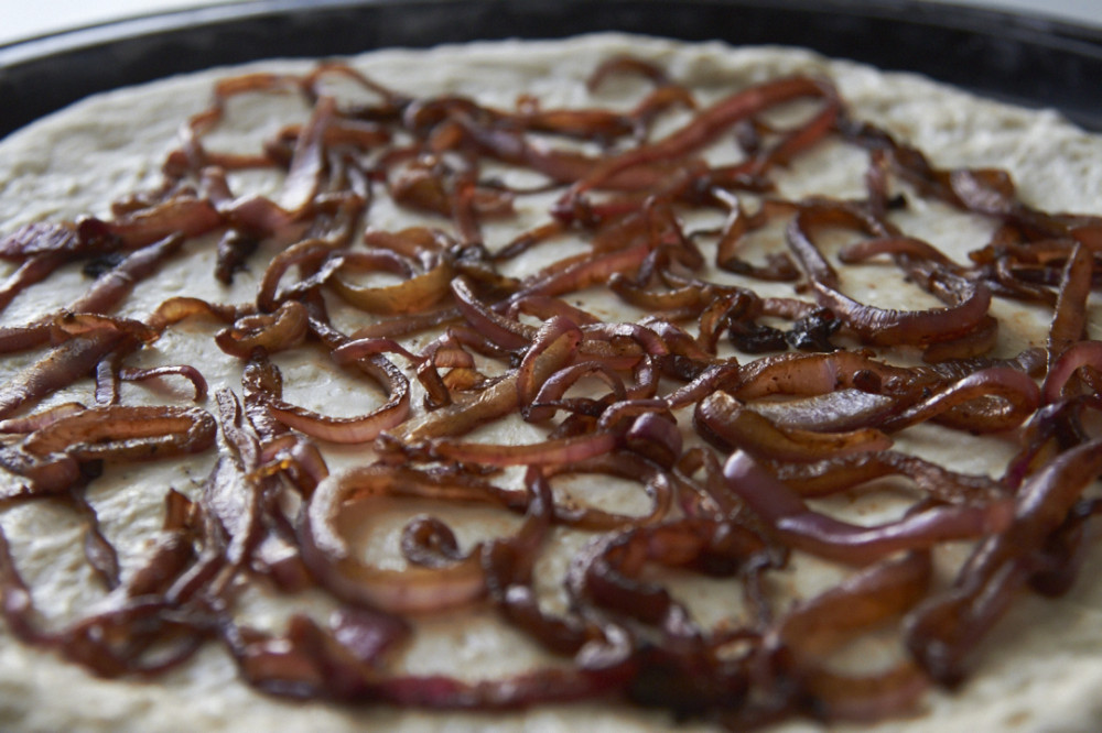 A raw pizza crust with caramelized onions on top.