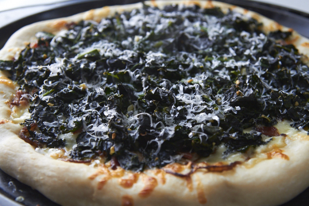 Cooked kale pizza topped with pecorino romano cheese.