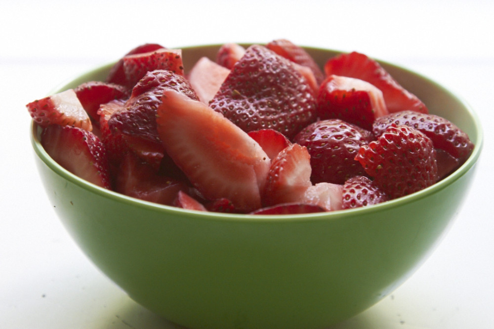 Sliced strawberries in a green bowl.