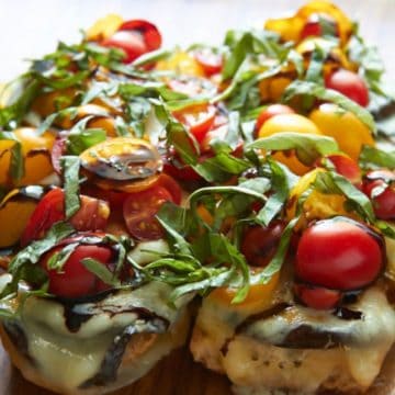 An open-faced eggplant sandwich topped with melted cheese, fresh tomatoes, and basil.