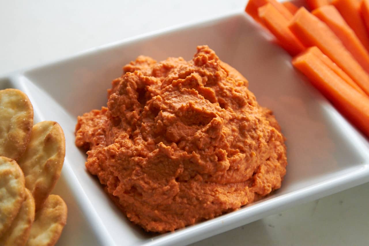 Creamy romesco dip in a dish with carrots and crackers.