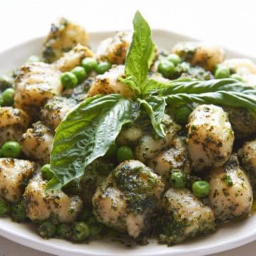 Gnocchi with peas and pesto topped with fresh basil on a white plate.