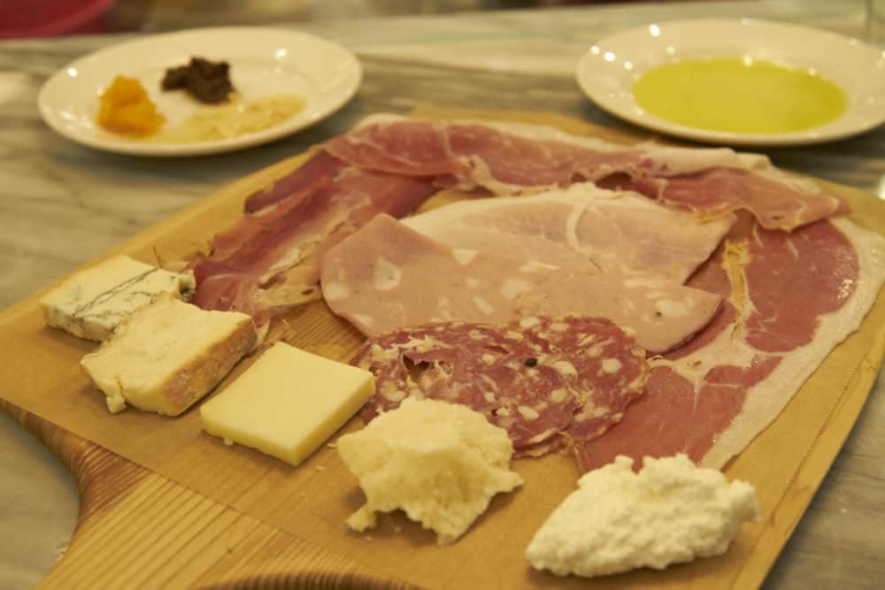 A plate of cheese and charcuterie served on a wooden plate at Eataly. 