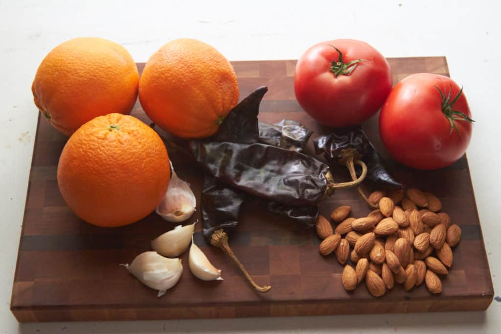Ingredients for almond orange mole sauce: oranges, tomatoes, guajillo chiles, almonds and garlic displayed on a cutting board.