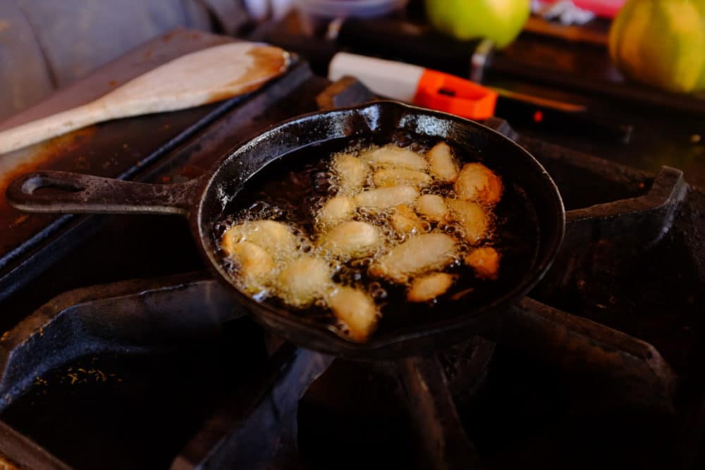 Almonds frying in a cast iron skillet on a large gas stovetop. 