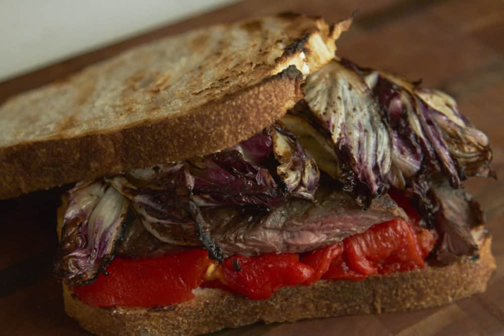 A steak sandwich with radicchio and red peppers on a wooden cutting  board.