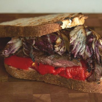 A steak sandwich with radicchio and red peppers on a wooden cutting board.