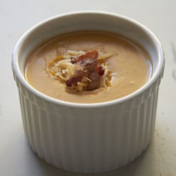 A small bowl of Beer Cheese Potato Soup, topped with crispy bacon and shredded cheese