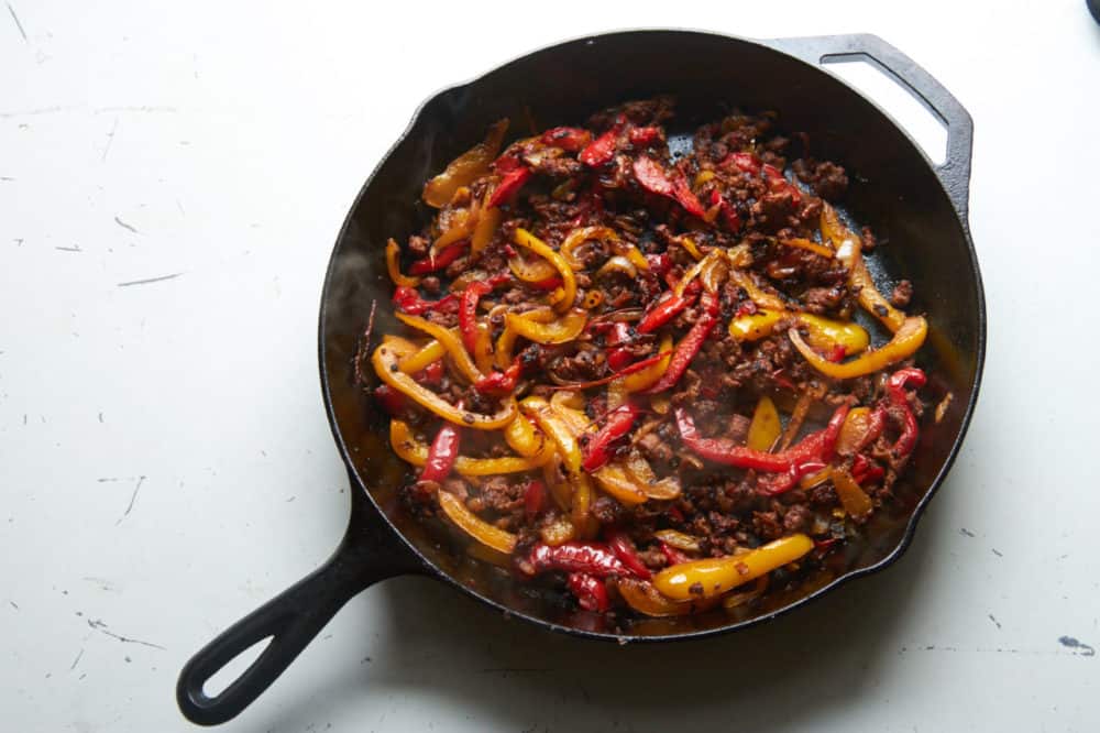 Cast iron skillet with red and yellow bell peppers, onions, and chorizo.