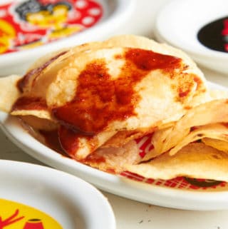 Paprika chips on a small plate surrounded by plates that are red, black and yellow with Spanish phrases written on them.