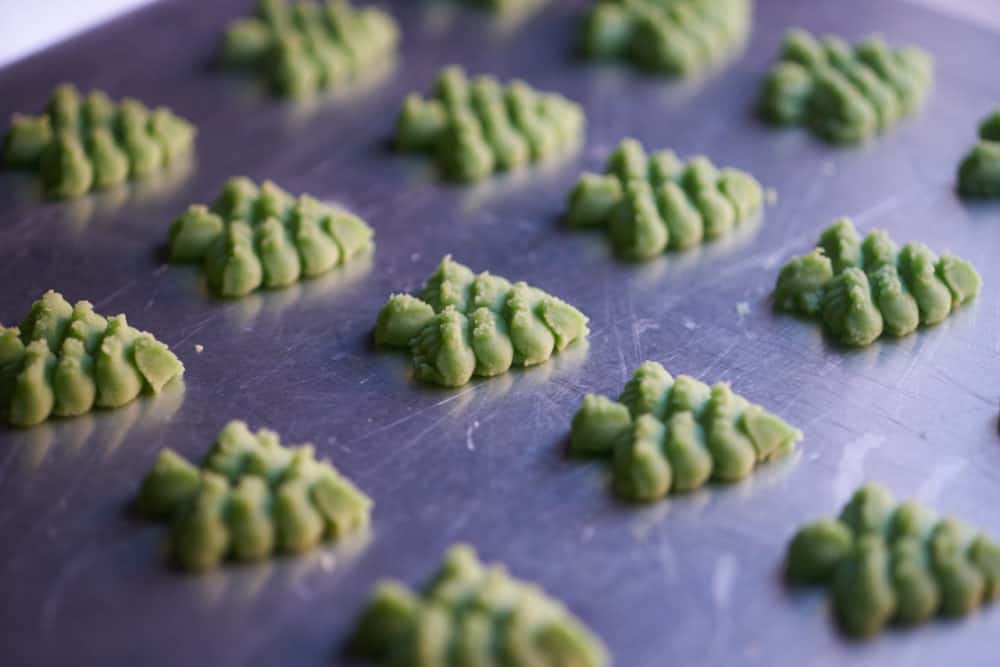 Side view of several green, Christmas tree shaped cookies on a silver baking sheet. 