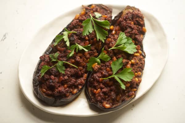 Stuffed-Eggplant-Lamb-PineNuts-Jan18-563 Eggplant stuffed with lamb and pine nuts, garhished with parsley on a white plate.