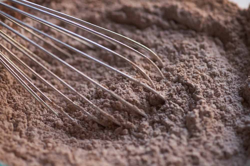 A wire whisk in a glass bowl with powdered sugar and cocoa powder mixed together.