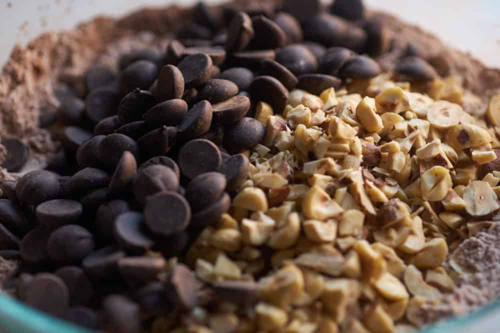 Chocolate chips and chopped hazelnuts on top of a bowl full of cocoa powder and powdered sugar.