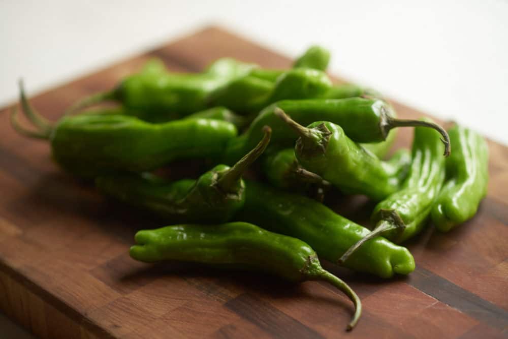 Shishito peppers on a wooden cutting board.