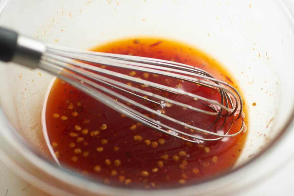 Sauce in a glass bowl with a whisk, displayed on a white surface.