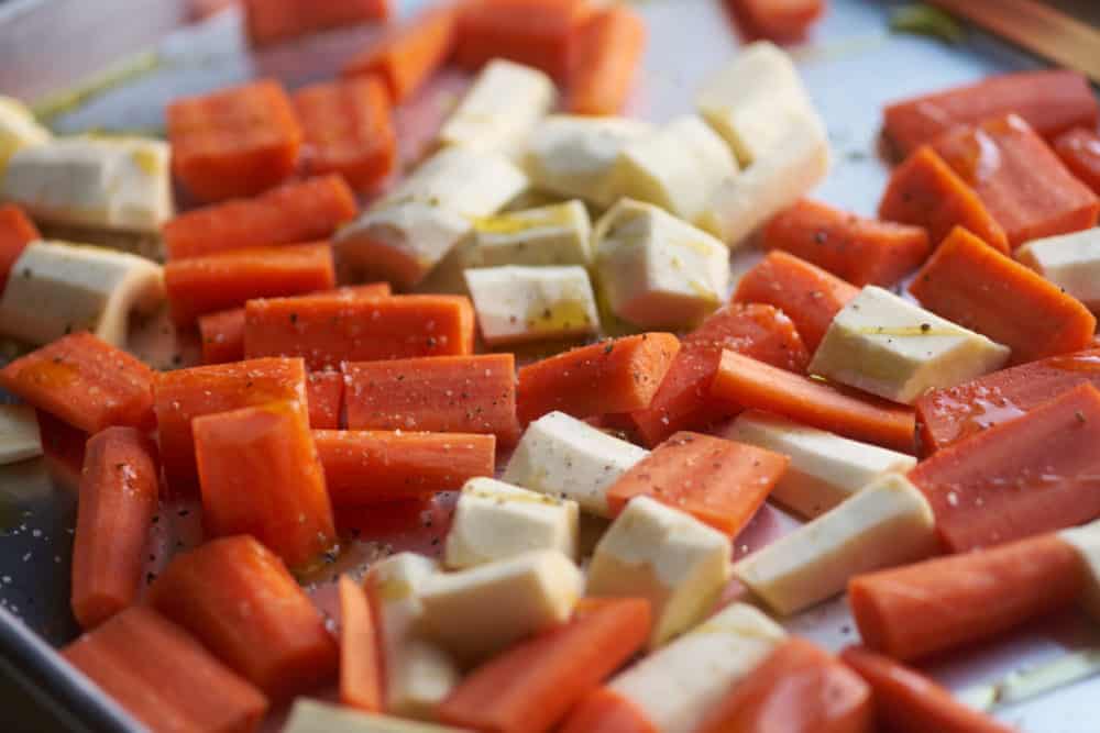 Sliced carrots and parsnips with olive oil and salt and pepper on a sheet pan.