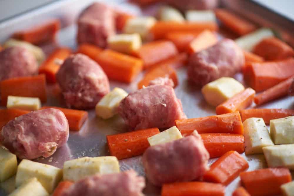 Chunks of Italian sausages on a sheet pan with carrots and parsnips.